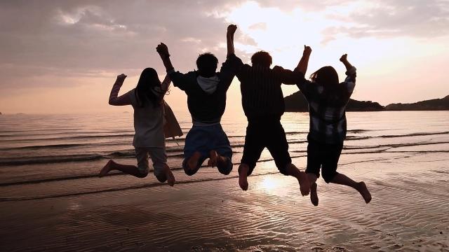 海岸の夕日を見て飛び跳ねる若者たちです。